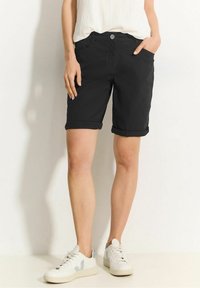 Schwarze, hochgekrempelte Shorts aus Baumwollmischung mit Taschen vorne und einem einzelnen Knopfverschluss. Kombiniert mit weißen Sneakern.