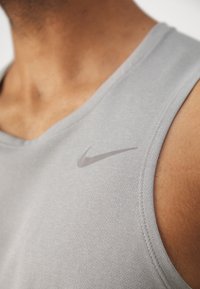 Nahaufnahme einer Person, die ein hellgraues Nike ärmelloses Sportoberteil trägt, mit sichtbarer Stoffstruktur und Logo auf der Brust.