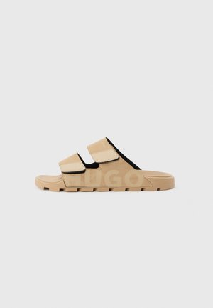 Beige slide sandal with two adjustable Velcro straps and a rugged sole, designed for casual wear.