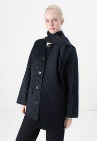 Marineblauer Wollmantel mit vertikalen Nadelstreifen, doppelt knöpfbarem Design, großen schwarzen Knöpfen und einem passenden Schal, der um den Hals gelegt ist.