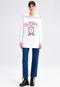 White sweatshirt with red lettering "CALIFORNIA," a sailor collar with contrasting trim, paired with blue straight-leg jeans and black boots.