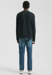 Zwarte langemouw shirt met een ronde hals, gecombineerd met blauwe denim jeans en witte sneakers, gezien van achteren.