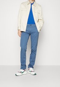 Beige knäppt skjorta, blå polo, blå byxor och flerfärgade sneakers med vit bas, gröna och burgundyröda accenter. Släta tyger och avslappnad passform.