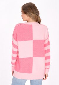 Maglione rosa con un motivo a quadretti e righe. Il design presenta diverse tonalità di rosa, un orlo a coste e un materiale morbido e testurizzato.