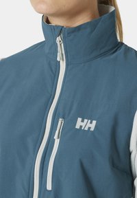 Chaqueta azul con un cuello alto, que presenta una cremallera blanca, acentos de forro polar y un logo bordado. Tejido texturizado con un acabado suave.