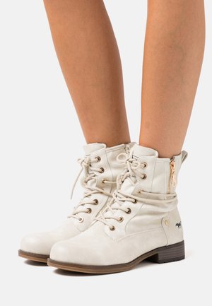 Cream ankle boots made of textured leather, featuring lace-up front, gold metal accents, and a side zipper for easy wear.