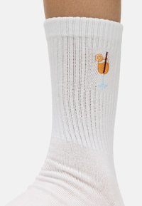 Calcetines blancos acanalados con un patrón de punto, que presentan un vaso de cóctel naranja bordado en el lado.