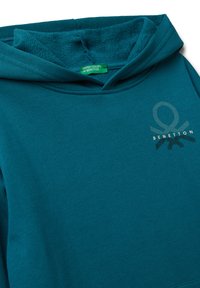 Tyrkysová mikina s kapucí s texturovaným vnitřkem, obsahující malé logo Benetton a zelenou etiketu "United Colors of Benetton" uvnitř límce.