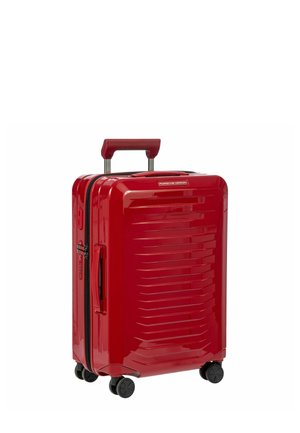 Roter Hartschalenkoffer mit glänzender Oberfläche, ausgestattet mit horizontalen Rillen, einem ausziehbaren Griff und vier schwarzen Rollen für einfache Mobilität.