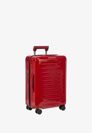 Valigia rigida rossa con finitura lucida, caratterizzata da scanalature orizzontali, manico retrattile e quattro ruote nere per una facile mobilità.