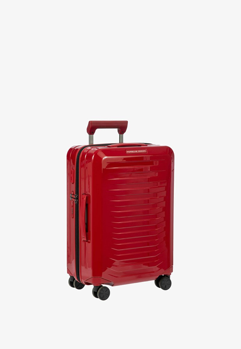 Roter Hartschalenkoffer mit glänzender Oberfläche, ausgestattet mit horizontalen Rillen, einem ausziehbaren Griff und vier schwarzen Rollen für einfache Mobilität.