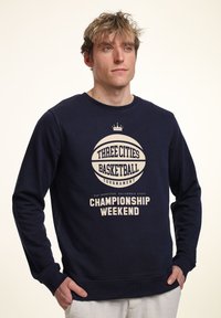 Navy Sweatshirt aus Baumwollmischung. Mit einem großen Basketball-Graphic und dem Text "Drei Städte Basketballturnier" sowie "Championship Wochenende."