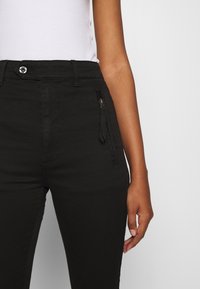Pantalones de tiro alto negros con detalle de bolsillo con cremallera, hechos de una tela suave, que cuentan con un cierre de botón y presillas para cinturón.