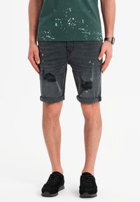 Shorts in denim grigio scuro con orli sfrangiati, dettagli consumati e risvolti. Abbinati a una maglietta verde a pois e scarpe da ginnastica nere.