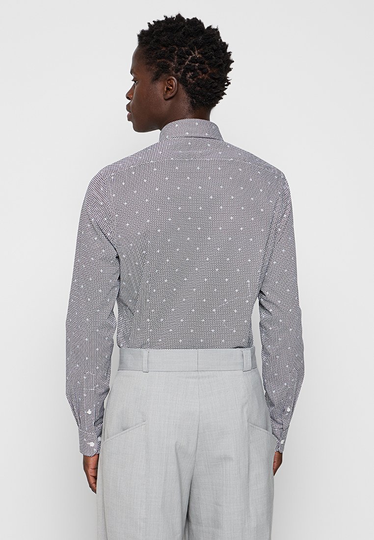 Camisa de botones en un micro patrón blanco y negro, con un ajuste entallado y mangas largas, combinada con pantalones gris claro con bolsillos laterales.