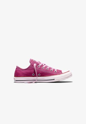 Lage roze canvas sneaker met witte rubberen zool, witte neuskap en roze veters, zijaanzicht op een witte achtergrond.