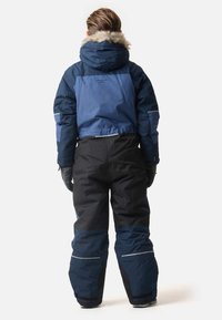 Blå och svart vinteroverall med huva, pälsdetaljer och reflexer. Designen inkluderar en kort topp och löst sittande byxor.