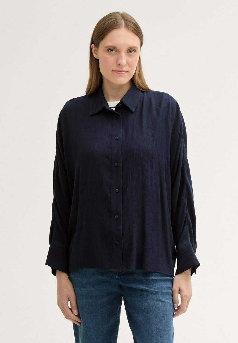 Donkerblauwe button-up shirt met een ontspannen pasvorm, lange mouwen en een textuurstof. Gecombineerd met blauwe jeans.