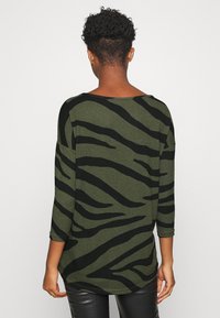 Grünes Strickoberteil mit schwarzen Zebrastrifen, Rollkragen, dreiviertel Ärmeln und lockerer Passform, aus weichem Stoff gefertigt.