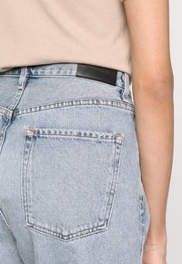 Jeans de mezclilla azul claro con cintura alta, que cuentan con dos bolsillos traseros, costuras en contraste y una etiqueta de marca de cuero negro en la cintura.