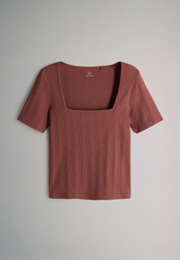 Top a maniche corte a coste color ruggine con scollatura quadrata ampia, posato disteso su uno sfondo grigio neutro.