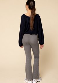 Zwarte, gemarmerde langemouwen top gecombineerd met grijs gestreepte flared broeken met zijsplits. Draagt schoenen van sportieve stijl. Neutraal achtergrond.