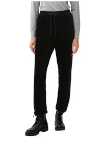 Pantalons en velours côtelé noirs avec une taille élastique, dotés de deux poches avant. Associés à des bottes noires à lacets, présentant une surface texturée.