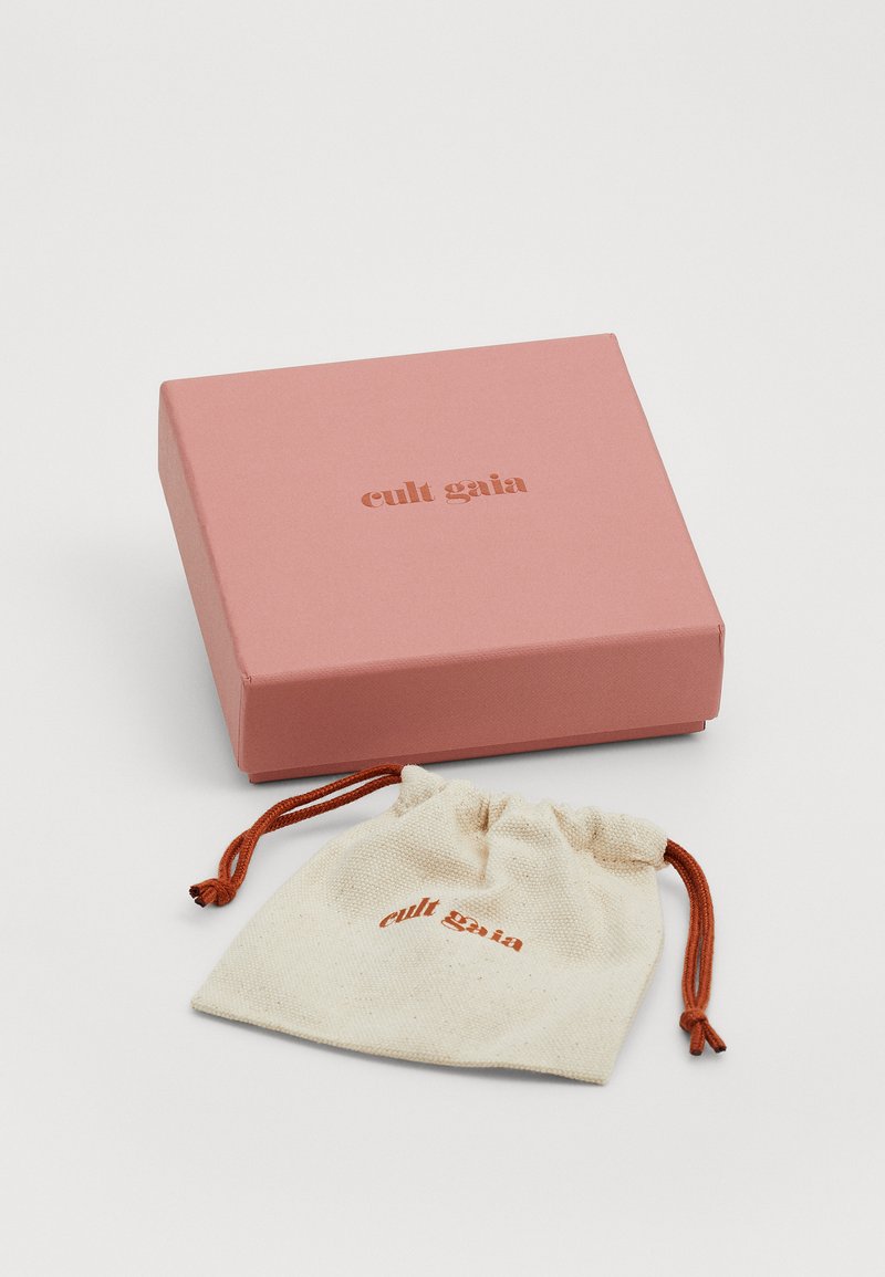 Rosa quadratische Box mit dem eingeprägten Schriftzug "cult gaia" in einem dunkleren Farbton, neben einem kleinen cremefarbenen Beutel mit Zugband, auf dem dasselbe Logo in Orange zu sehen ist.