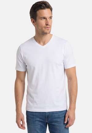Mann trägt schlichtes weißes V-Ausschnitt-T-Shirt mit kurzen Ärmeln und blaue Jeans, schaut leicht zur Seite vor weißem Hintergrund.