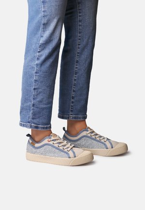 Szare i niebieskie trampki z chropowatym materiałem na cholewce, kremowymi akcentami oraz żeberkowaną podeszwą, noszone z niebieskimi podwiniętymi dżinsami.