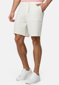 Pantalones cortos blancos texturizados con cintura ajustable, que cuentan con dos bolsillos frontales y un corte recto, combinados con zapatillas blancas.
