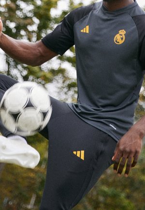 Henkilö, joka pukeutunut mustiin urheiluvaatteisiin, joissa on Real Madridin logo, jongleeraa mustavalkoista jalkapalloa ulkona.