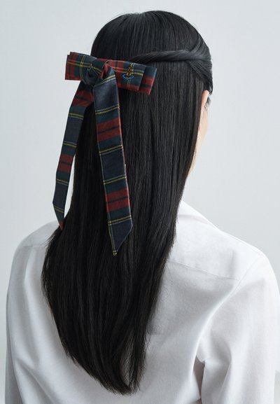 Sarkans, tumši zils un zaļš overspējošs audums matu lentā ar dekoratīvu mezglu. Gluda, taisna melna matu virkne krīt pār baltu krekliņu.