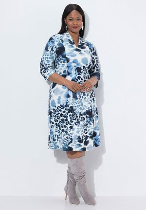 Blaues Kleid mit Blumenmuster und Dreiviertelärmeln, knielang, in einer Mischung aus Dunkel- und Hellblau; kombiniert mit grauen kniehohen Stiefeln.