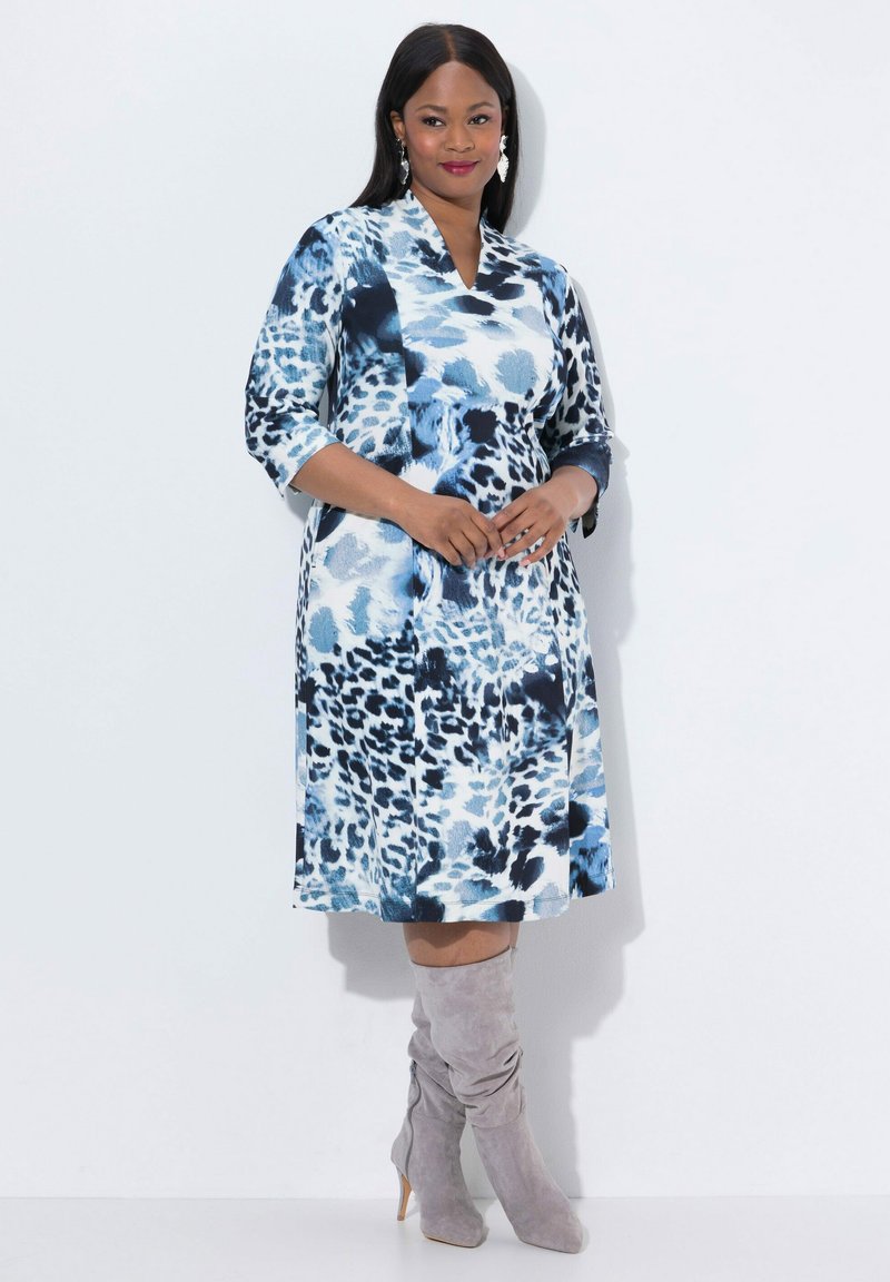 Blaues Kleid mit Blumenmuster und Dreiviertelärmeln, knielang, in einer Mischung aus Dunkel- und Hellblau; kombiniert mit grauen kniehohen Stiefeln.