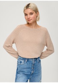Maglione beige a coste con maniche lunghe e scollo rotondo, abbinato a jeans di denim blu a vita alta con chiusura a bottoni e due tasche frontali.