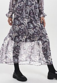 Lång, flödande klänning med ett mörkt blommigt paisleymönster, tillverkad av lätt, genomskinligt tyg. Har volangärmar och en flerlagers kjol.