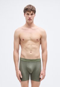 Ανδρικά μποξεράκια σε ελιά πράσινο, κατασκευασμένα από μαλακό, ελαστικό ύφασμα. Διαθέτουν εφαρμοστή γραμμή και φαρδιά ελαστική μέση με λογότυπο.