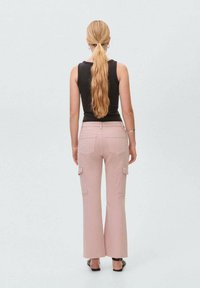 Roze cargo broek met brede pijpen en een hoge taille, voorzien van zijzakken en achterzakken. Gedragen met een zwarte mouwloze top.