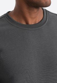 Felpa grigia scura caratterizzata da un collo a coste, texture morbida e design senza cuciture. Nessun logo o motivo visibile.