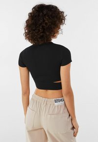 Svart ribbad crop top med korta ärmar och ett utskärningsdetalj. Kombineras med beigefärgade cargobyxor med en synlig varumärkesetikett.