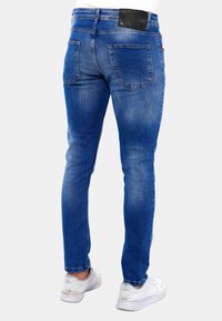 Blauwe denim skinny jeans met twee achterzakken, lichte vervaging en een zwart leren label bij de tailleband. Draag het met witte sneakers.