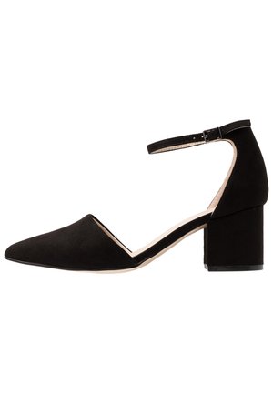 Zapato de tacón cuadrado de ante negro con punta afilada y correa en el tobillo; presenta una textura suave y un diseño minimalista.
