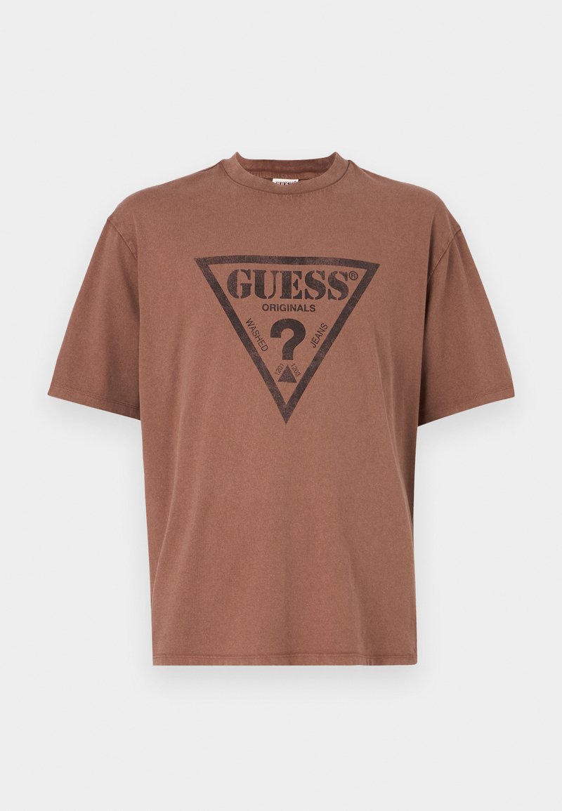 Brun bomullst-shirt med rund hals. Har en djärv svart triangulär logotypdesign med texten "GUESS ORIGINALS" och detaljer.