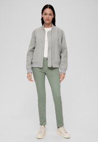 Szara kurtka bombowiec z zamkiem błyskawicznym, prążkowanymi mankietami i dolnym brzegiem. Połączona z jasnoszarymi spodniami i beżowymi trampkami. Pod spodem gładki biały T-shirt.