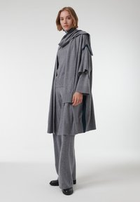 Conjunto de punto gris que presenta una blusa drapeada con un cuello de chal y mangas anchas, combinada con pantalones holgados y detalles oscuros.