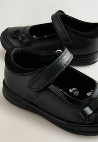 Schwarze Leder-Mary-Jane-Schuhe mit runder Zehenform, flachem Absatz, Klettverschluss und dekorativem Schleifendetail. Weiches Futter und strapazierfähige Gestaltung.