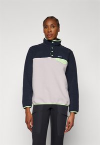 Fleece-pullover i marineblå og lys grå med grønne detaljer, har høy krage, trykknapper og brystlomme. Myk tekstur.