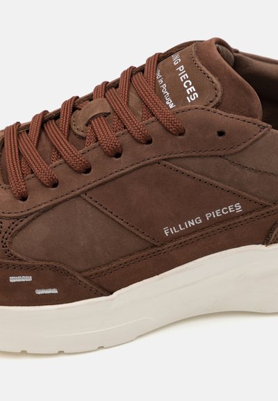 Hnědé semišové tenisky s texturovaným povrchem, s hnědými tkaničkami, bílou podrážkou a logem "FILLING PIECES" na boku.
