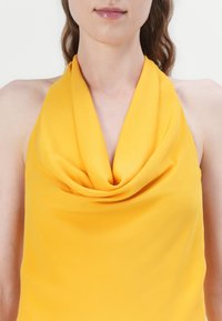 Haut halter jaune avec un décolleté drapé, fabriqué à partir d'un tissu lisse, présentant une coupe décontractée et sans coutures ni accents visibles.